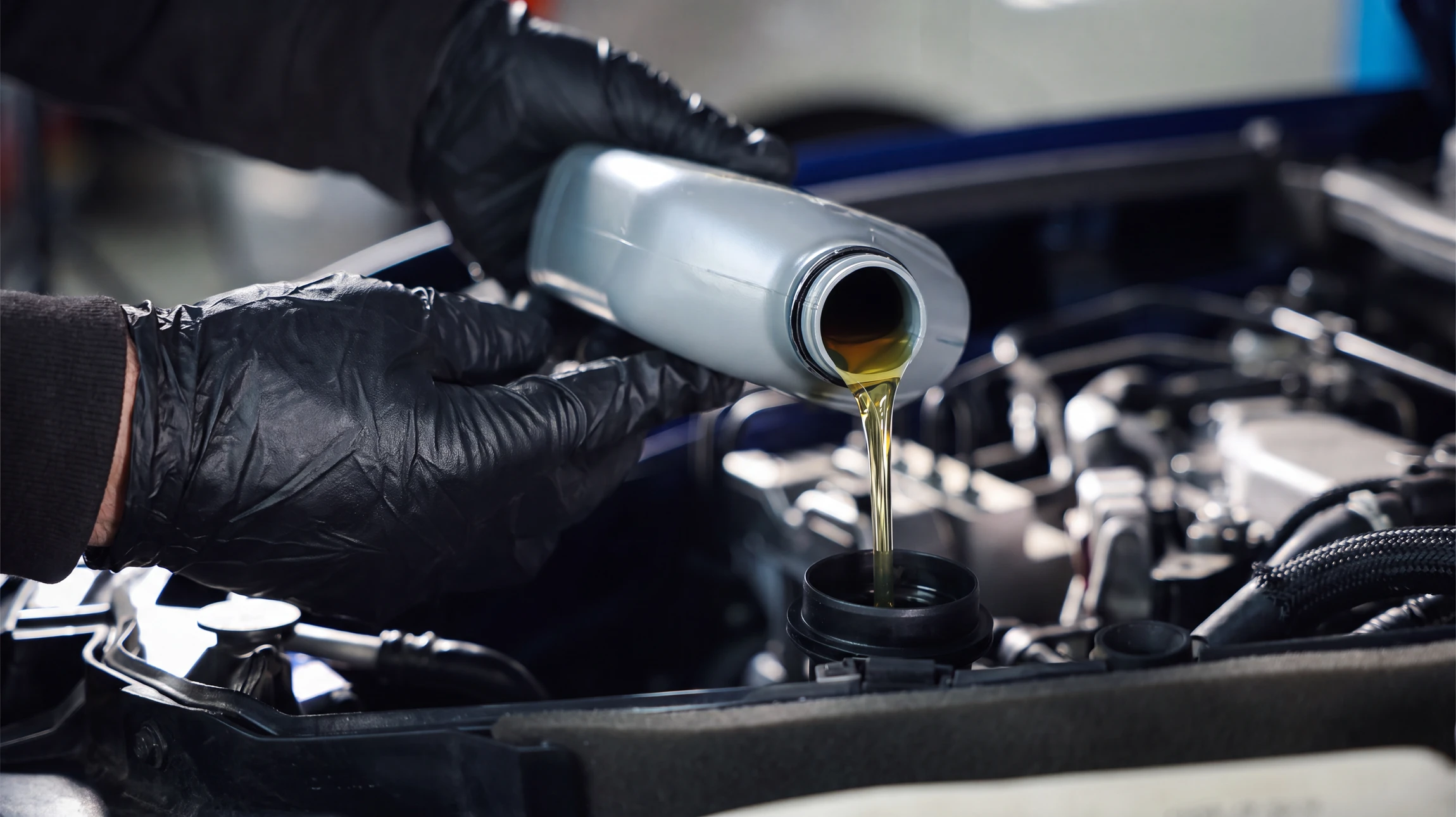 Mécanicien automobile en combinaison bleue examine le moteur d'un véhicule noir, capot ouvert dans un garage professionnel